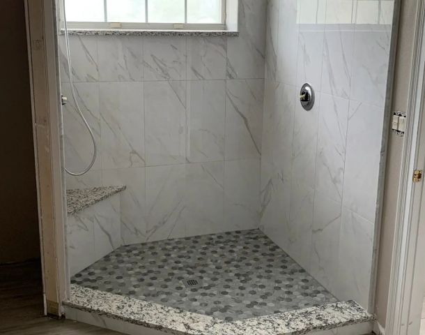Compact marble-look shower with a dark pebble mosaic floor and polished stone curb.