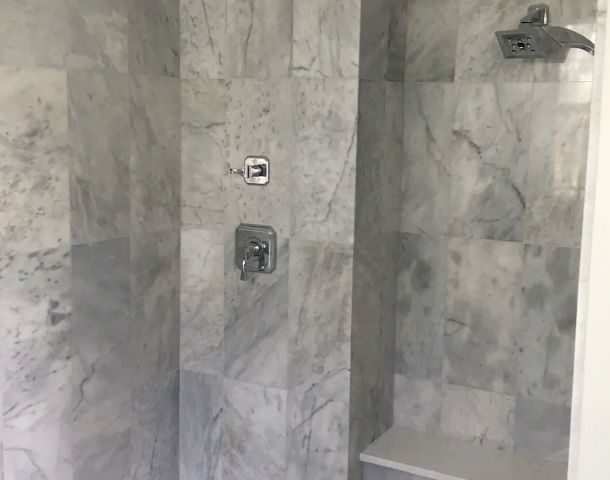 Gray marble walk-in shower with a built-in bench, recessed niche, and mosaic floor.
