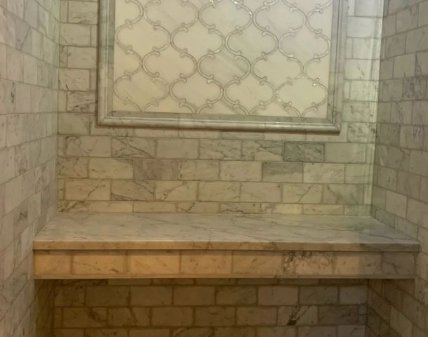 Gray marble-tiled shower with a built-in bench, framed window panel, and penny mosaic floor.