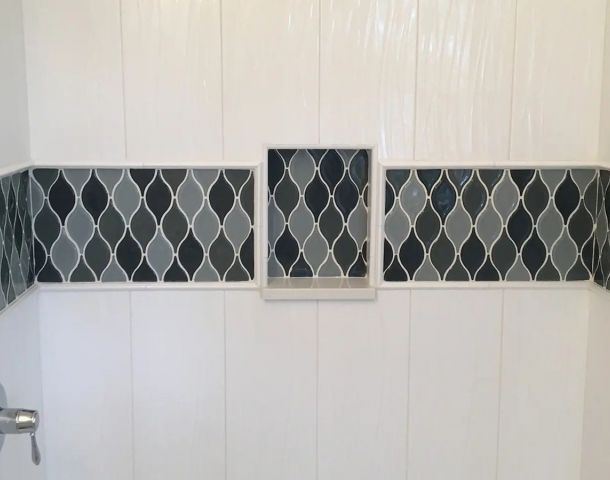 White tub surround with a dark diamond mosaic accent band and framed niche.