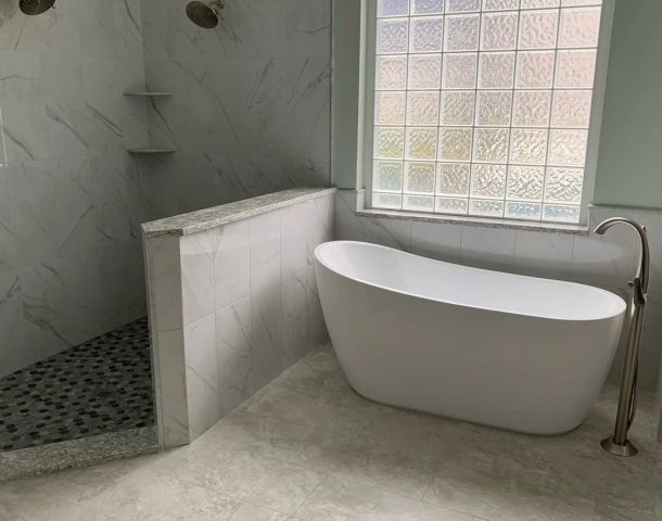 Freestanding tub beside a marble-look walk-in shower with a pebble mosaic floor.